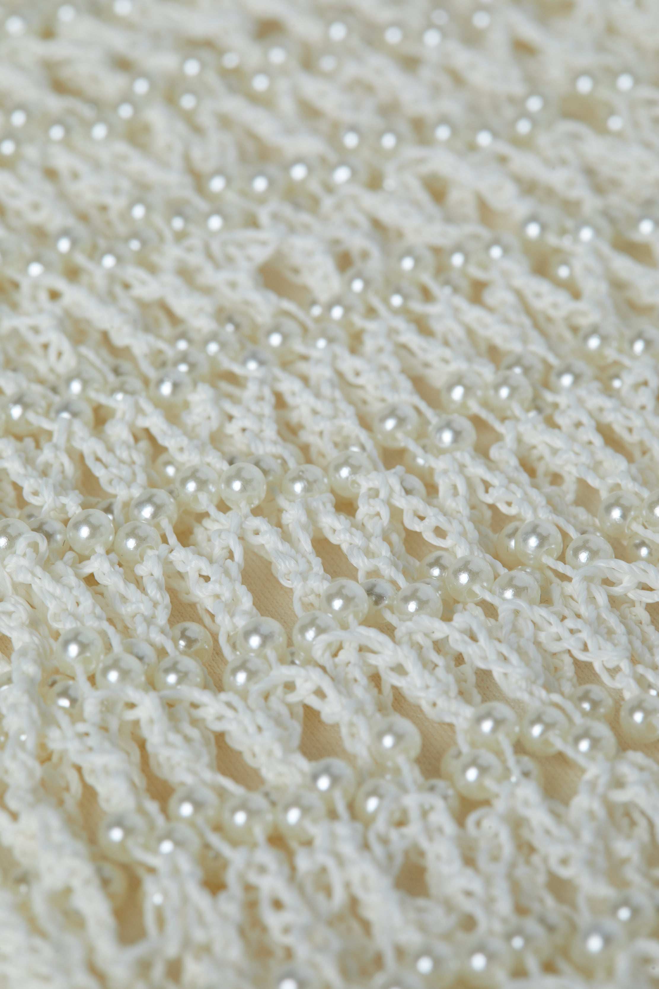 Close-up of the Angela Crochet Cover-Up Dress, featuring a white crocheted fabric with an open, lacy pattern, decorated with evenly spaced small, shiny faux pearl accents throughout the design.