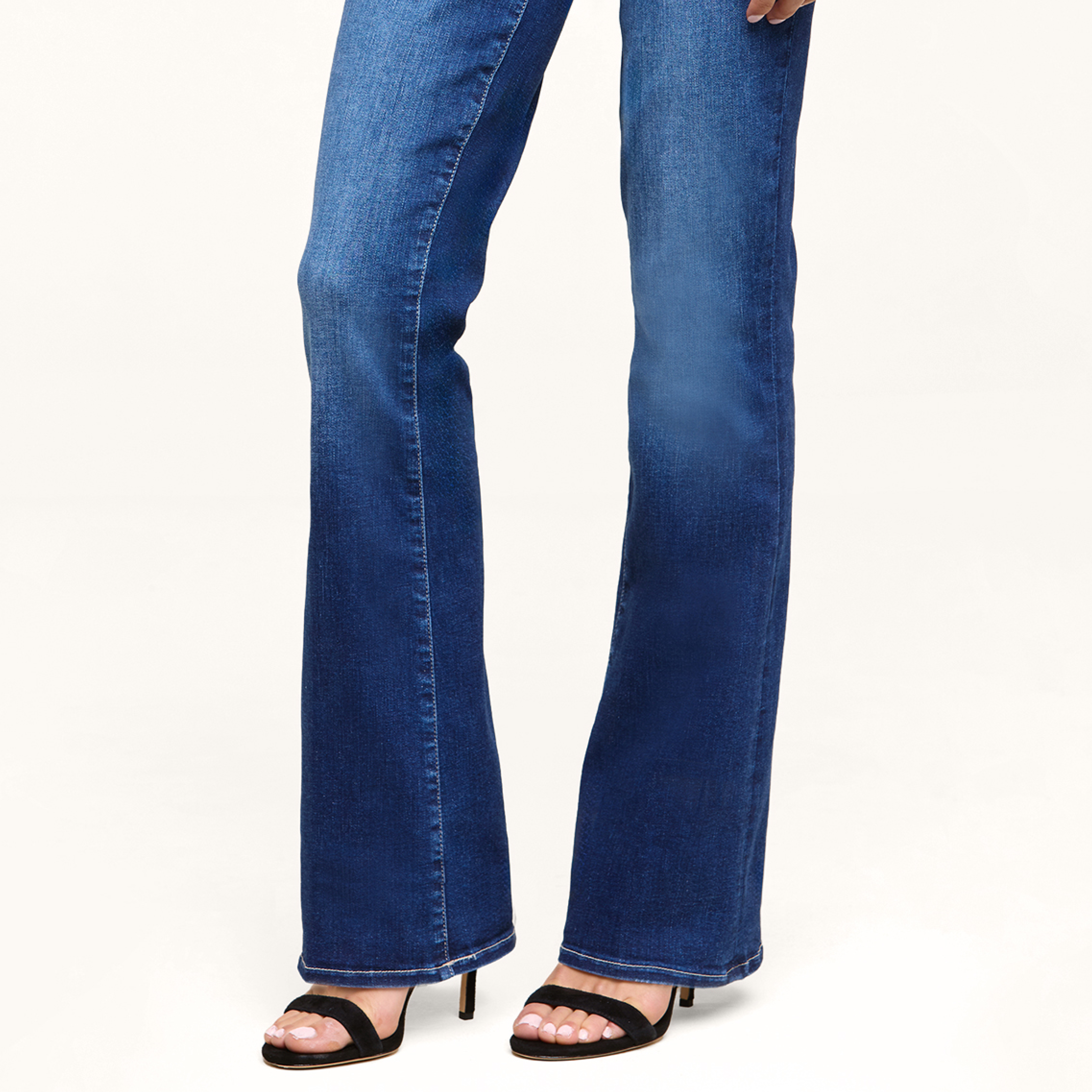 Person wearing dark blue bootcut jeans with black open-toe heels, standing on a light-colored surface. Only the lower half of the body is visible.