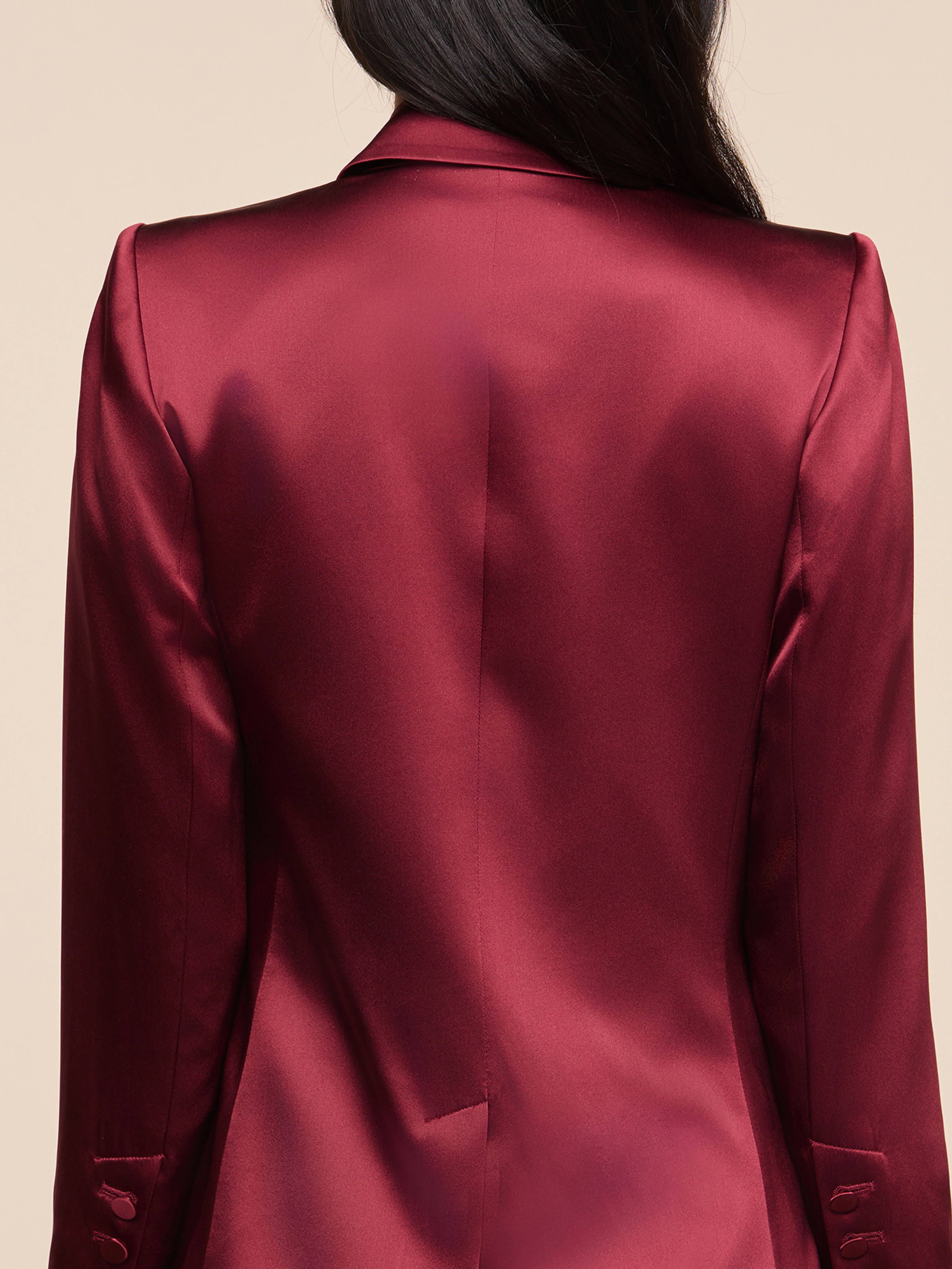 A person with long dark hair is shown from behind, wearing a shiny burgundy blazer with buttons on the sleeves, against a neutral background.