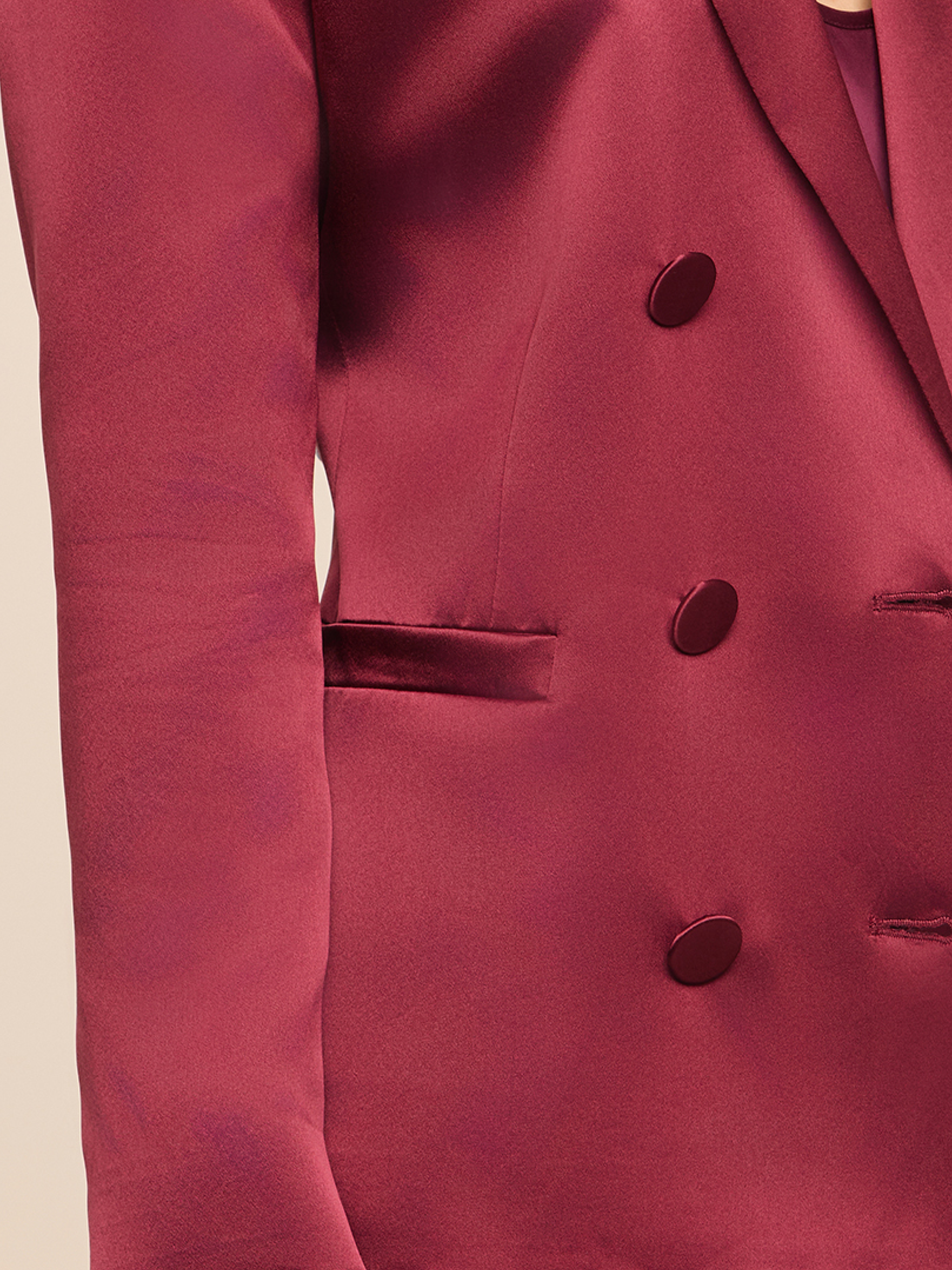 A close-up of a person wearing a shiny burgundy blazer with matching buttons. The fabric appears smooth and satin-like, with a visible pocket and part of the left arm and torso shown.