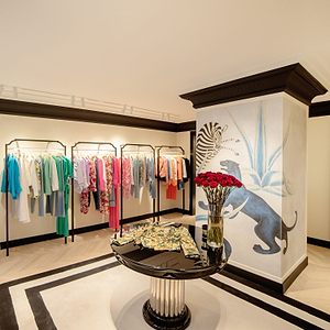 Designer clothing store interior with racks of clothes, a table with flowers, and decorative wall art.