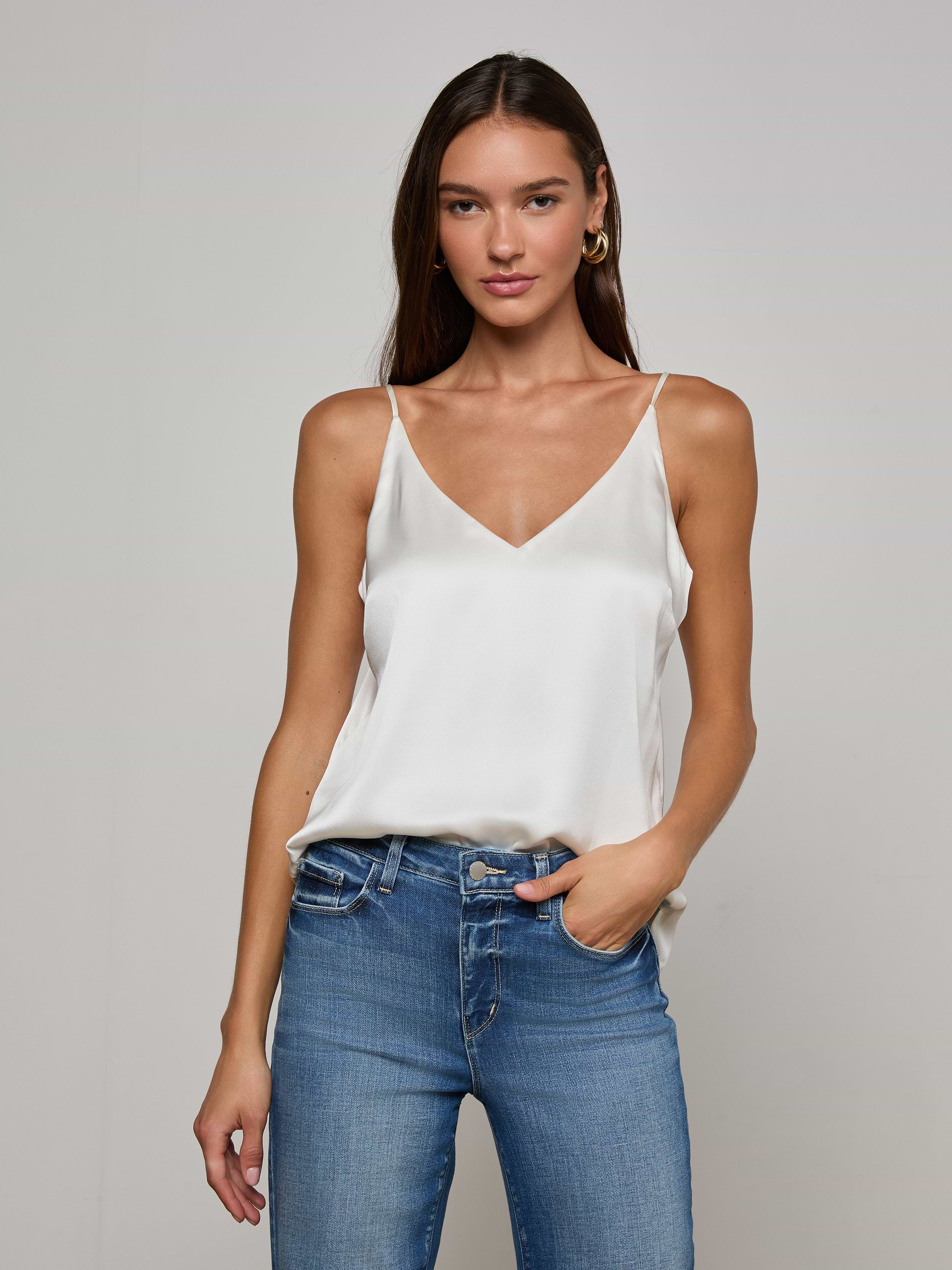 Model wearing the Gabriella Silk Camisole in ivory, paired with blue jeans, stands against a plain light background with one hand in her pocket and a relaxed expression.