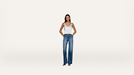 A woman stands with her hands in her pockets, wearing a white sleeveless top and blue jeans against a plain white background.
