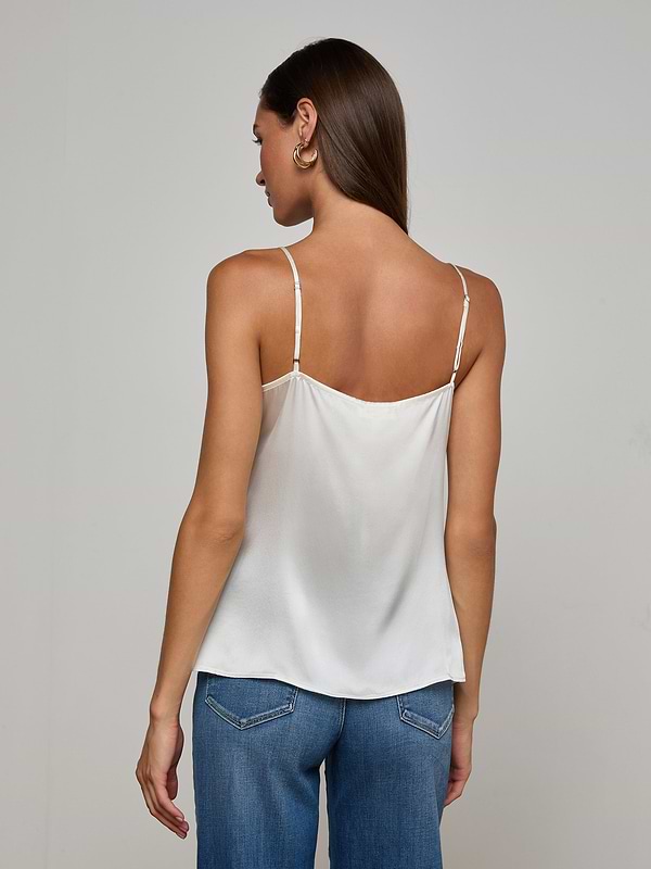 A woman with straight brown hair is facing away, wearing the Gabriella Silk Camisole in ivory with thin straps and blue jeans. The background is plain and light-colored.