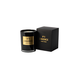 A black Ambre Soleil candle, adorned with gold accents and matching label, is displayed next to its coordinating black and gold box on a light background. This sophisticated candle is part of our hand-poured collection, thoughtfully crafted for a clean, even burn.