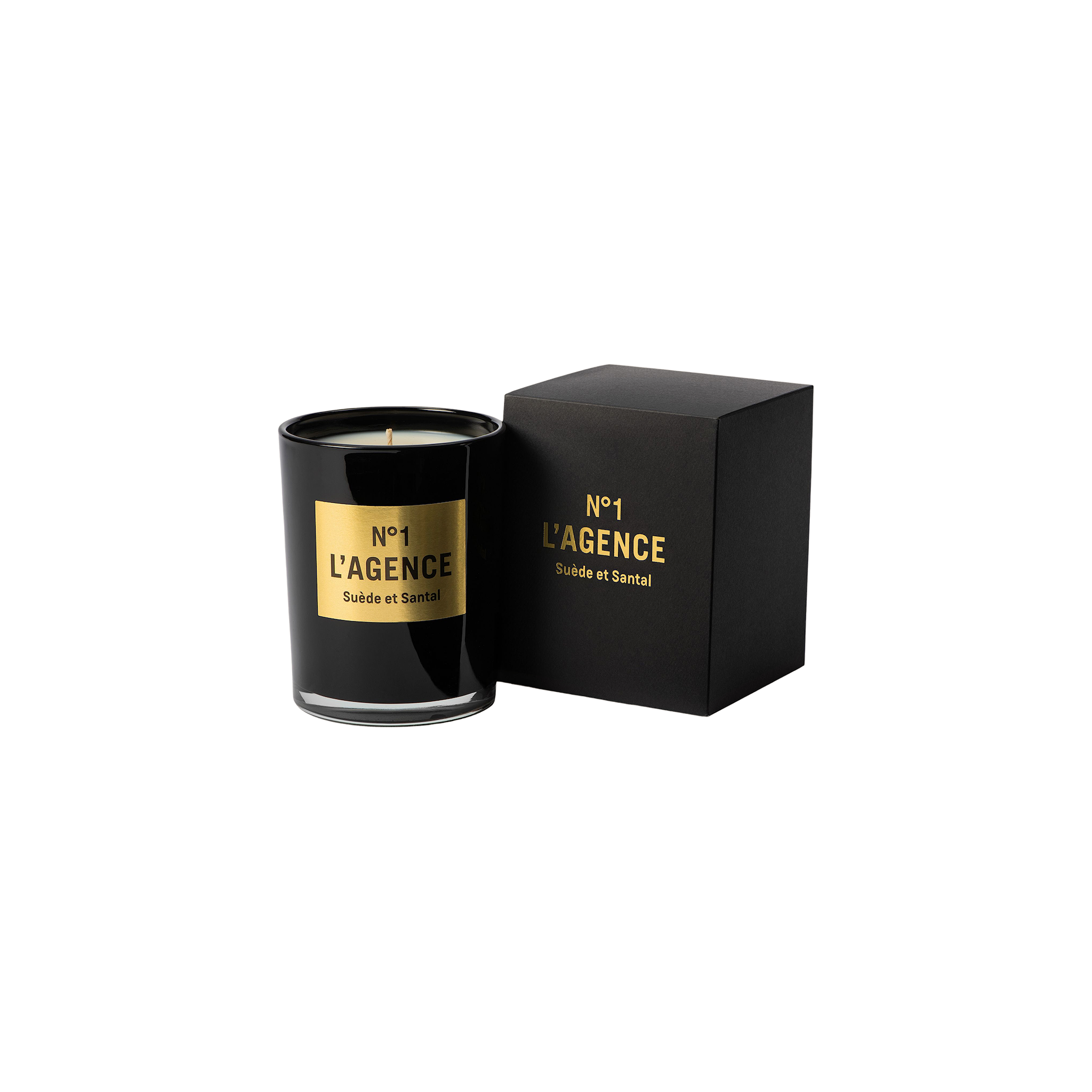 A black glass candle labeled Suède et Santal, made with soy-blend wax, sits next to its matching black and gold box on a plain white background.