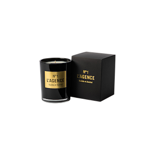 A black Suède et Santal candle with gold lettering sits beside its matching black and gold box, both displayed on a plain white background. This hand-poured Southern California soy-blend wax candle brings a sophisticated touch to any space.