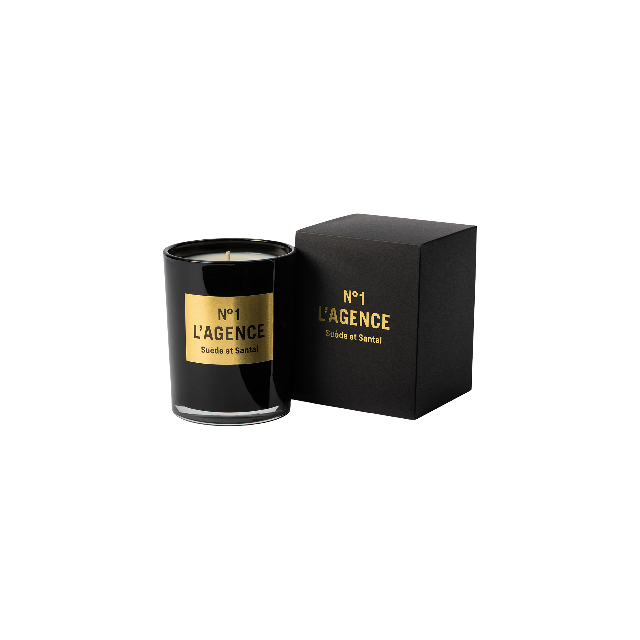 A black glass candle labeled Suède et Santal, made with soy-blend wax, sits next to its matching black and gold box on a plain white background.