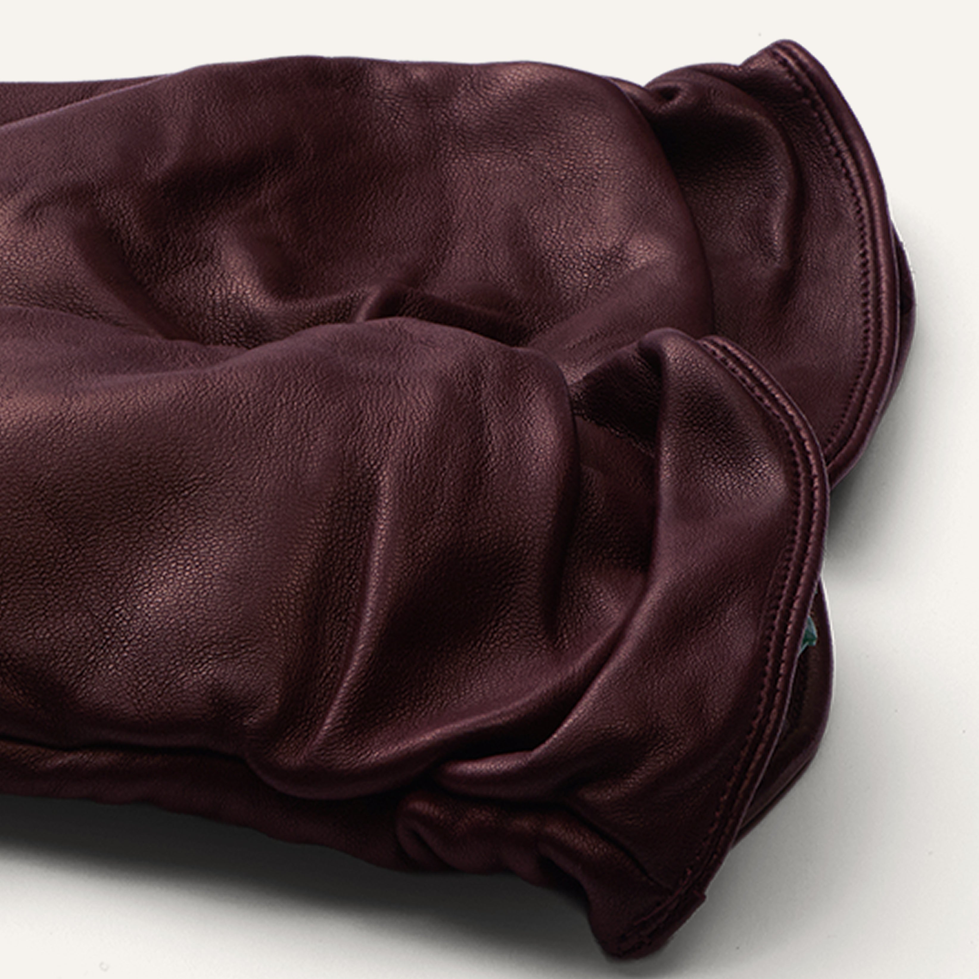 A pair of burgundy leather gloves rests on a neutral surface, their supple texture and elegant, soft folds highlighting the craftsmanship of the material.