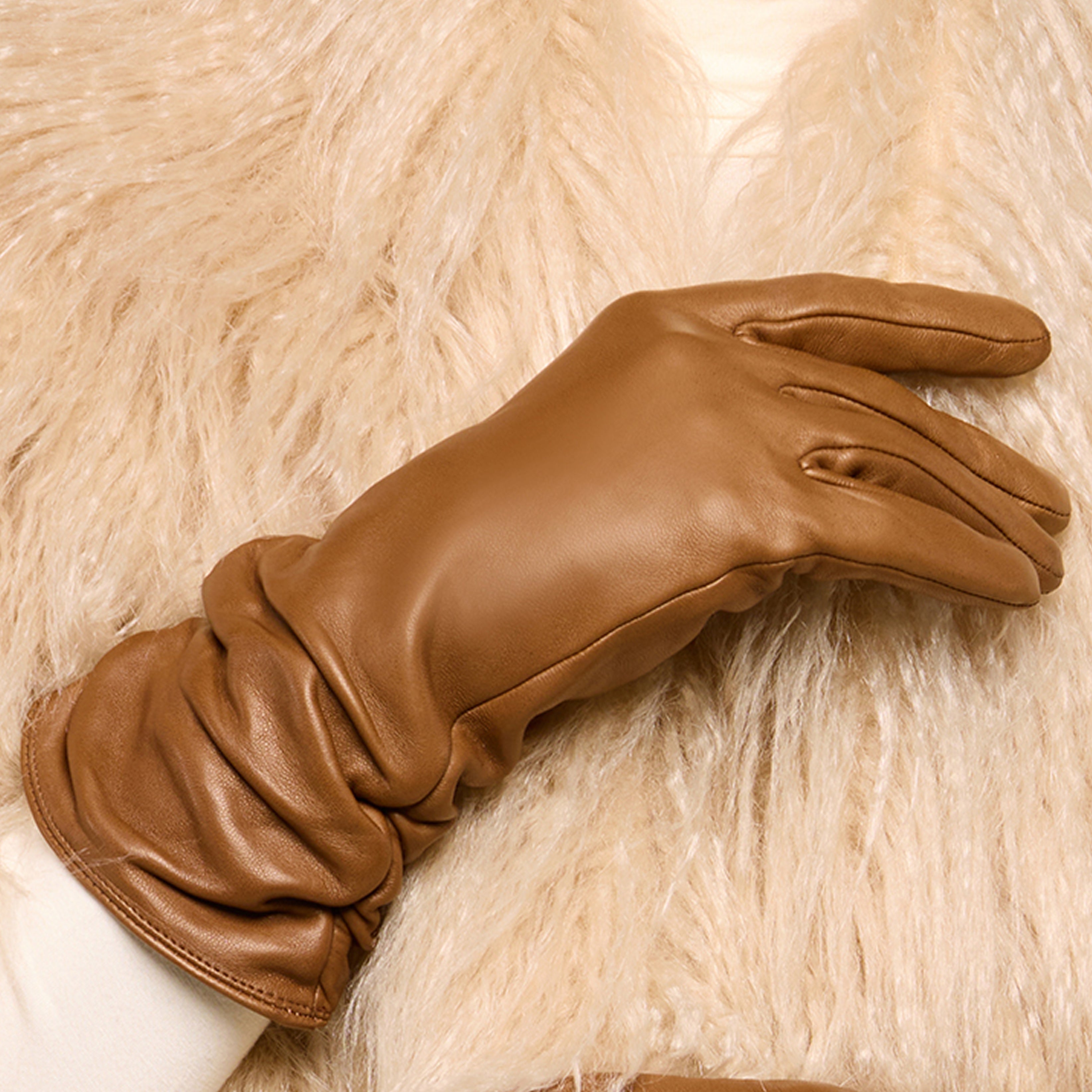 A person wearing a tan leather glove and a cream-colored faux fur coat, with the gloved hand resting near the chest.