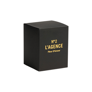 A sleek black rectangular box with gold text reading N°2 LAGENCE Fleur D’Amour on the front is displayed against a plain white background. The sophisticated packaging reflects the luxurious baccara rose fragrance and premium soy-blend wax featured in each hand-poured Fleur D’Amour candle.