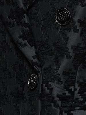 Close-up of a dark, textured blazer with a geometric pattern and two shiny black buttons. The fabric shows a mix of matte and glossy finishes, highlighting the intricate design.