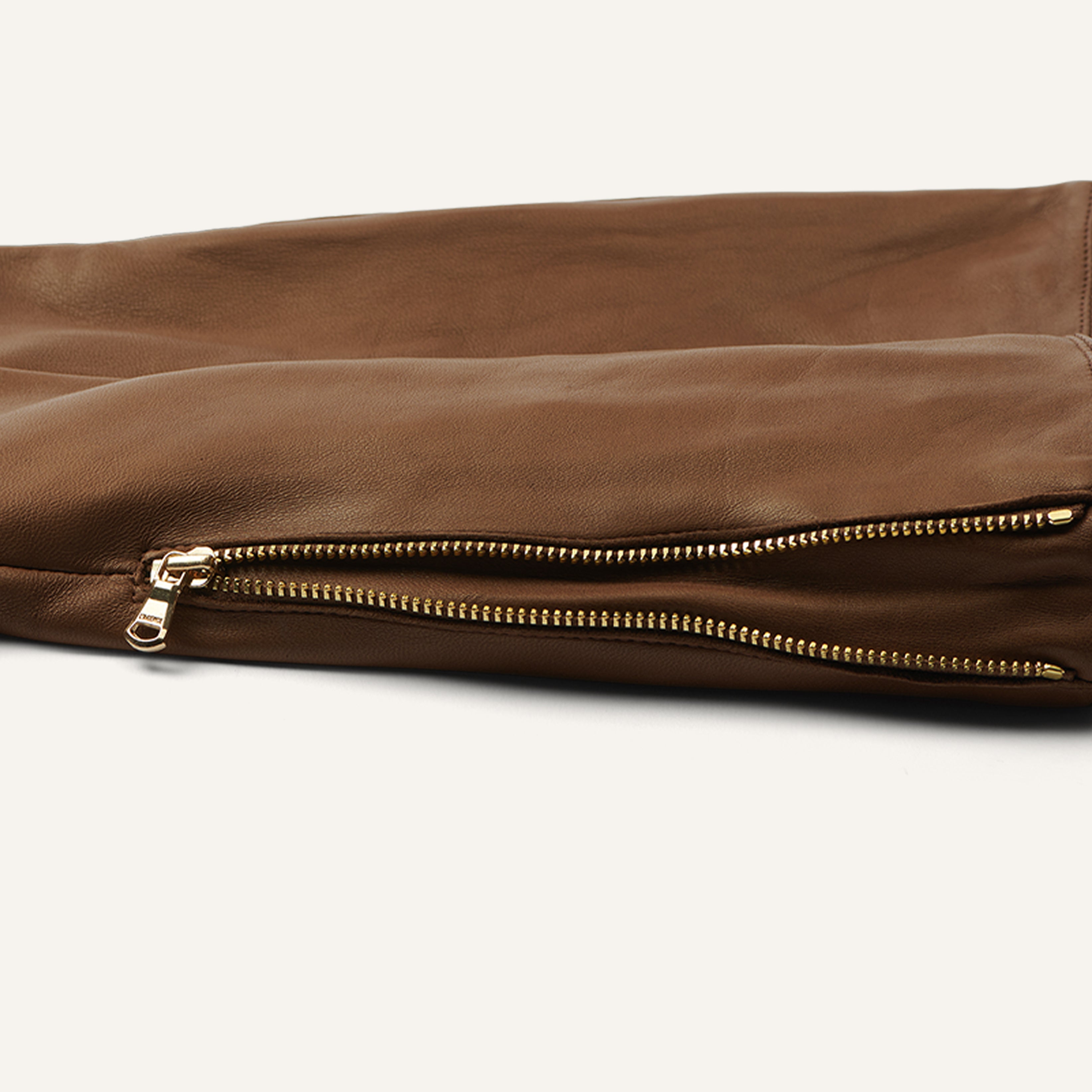 Close-up of a brown leather garment sleeve featuring two parallel gold zippers with pulls, showcased against a light background.