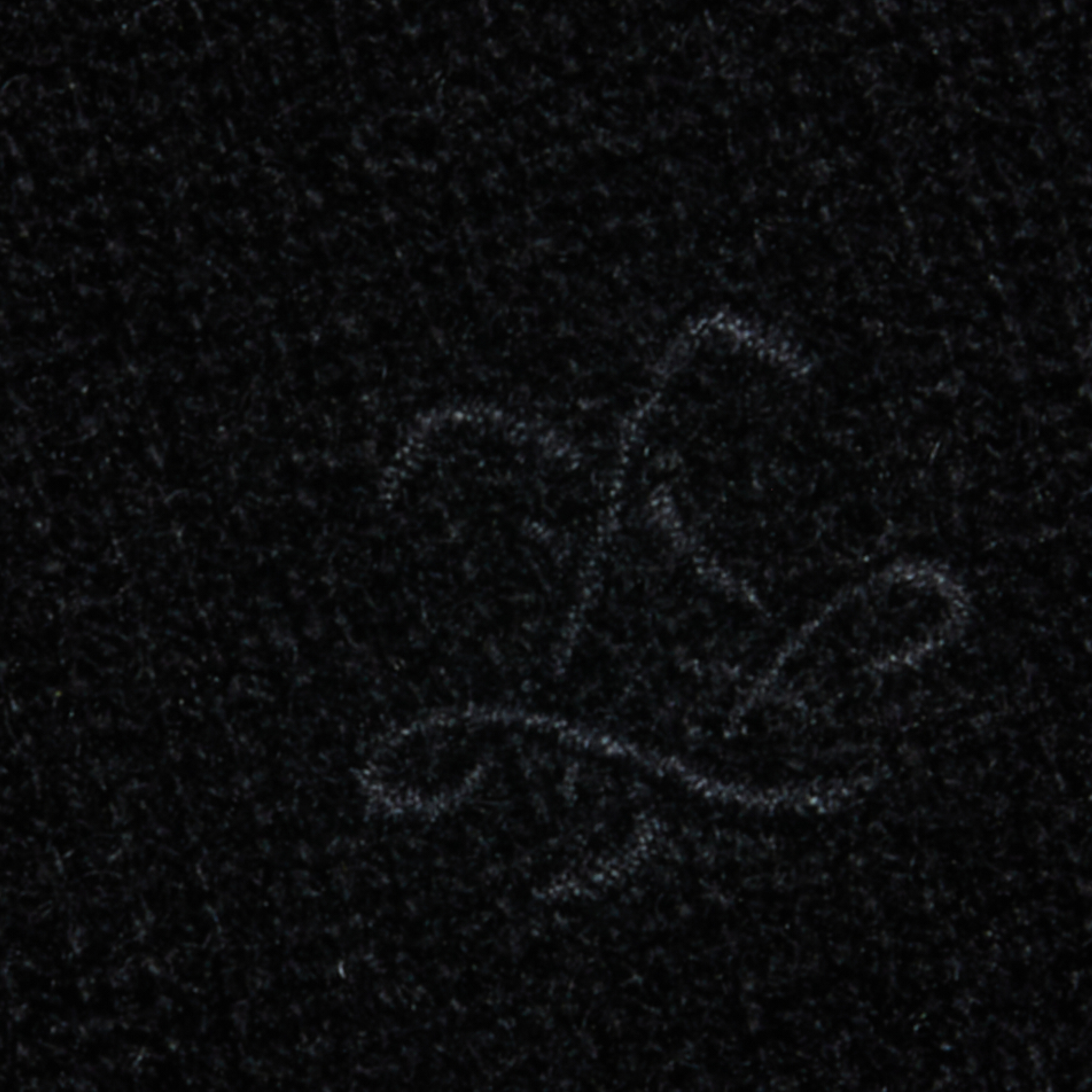 Close-up of a dark textured fabric, highlighted by a faint, embroidered cursive letter L in light thread at the center.