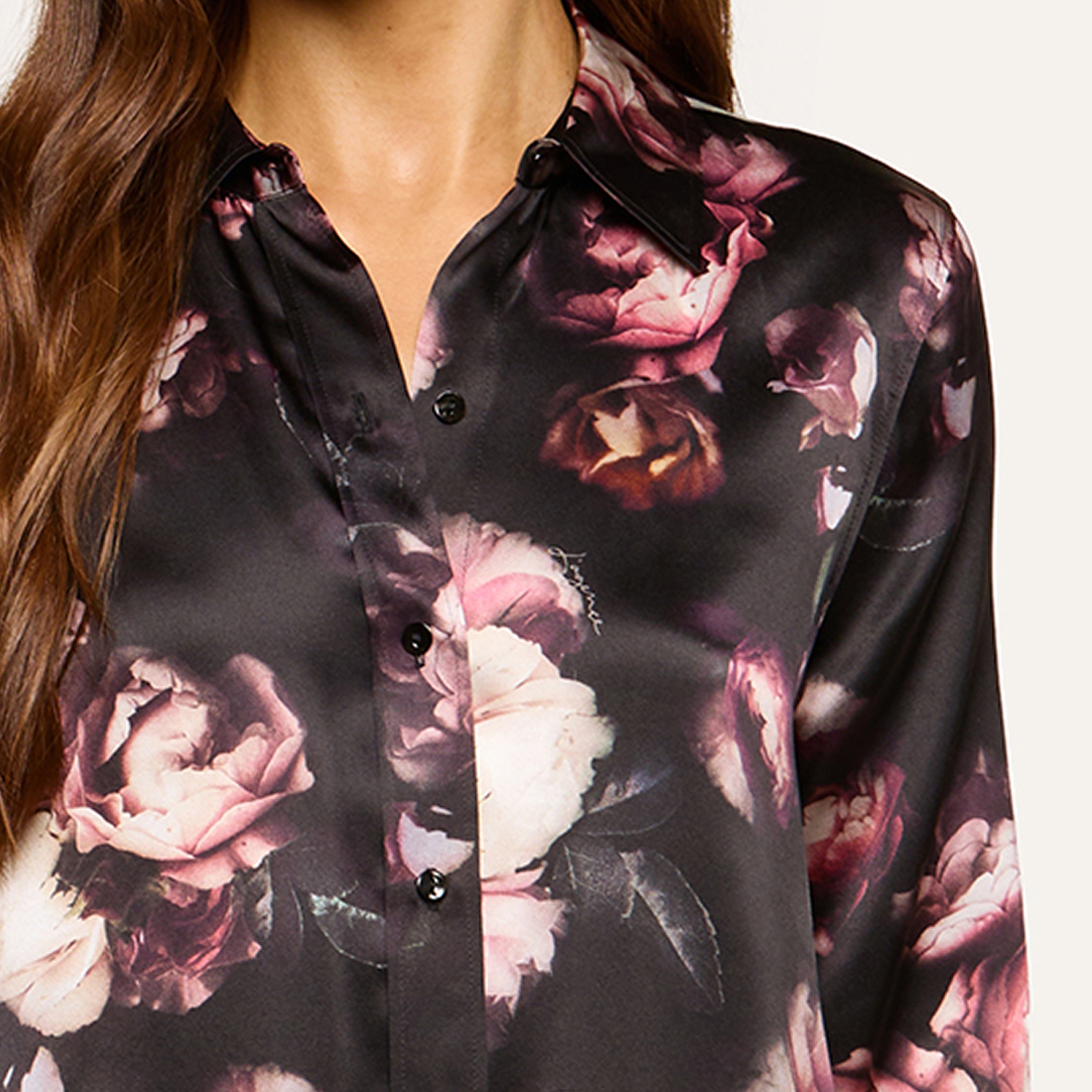 A woman wears a black satin shirt adorned with a pink and white floral print; the image shows her from the shoulders to the waist.