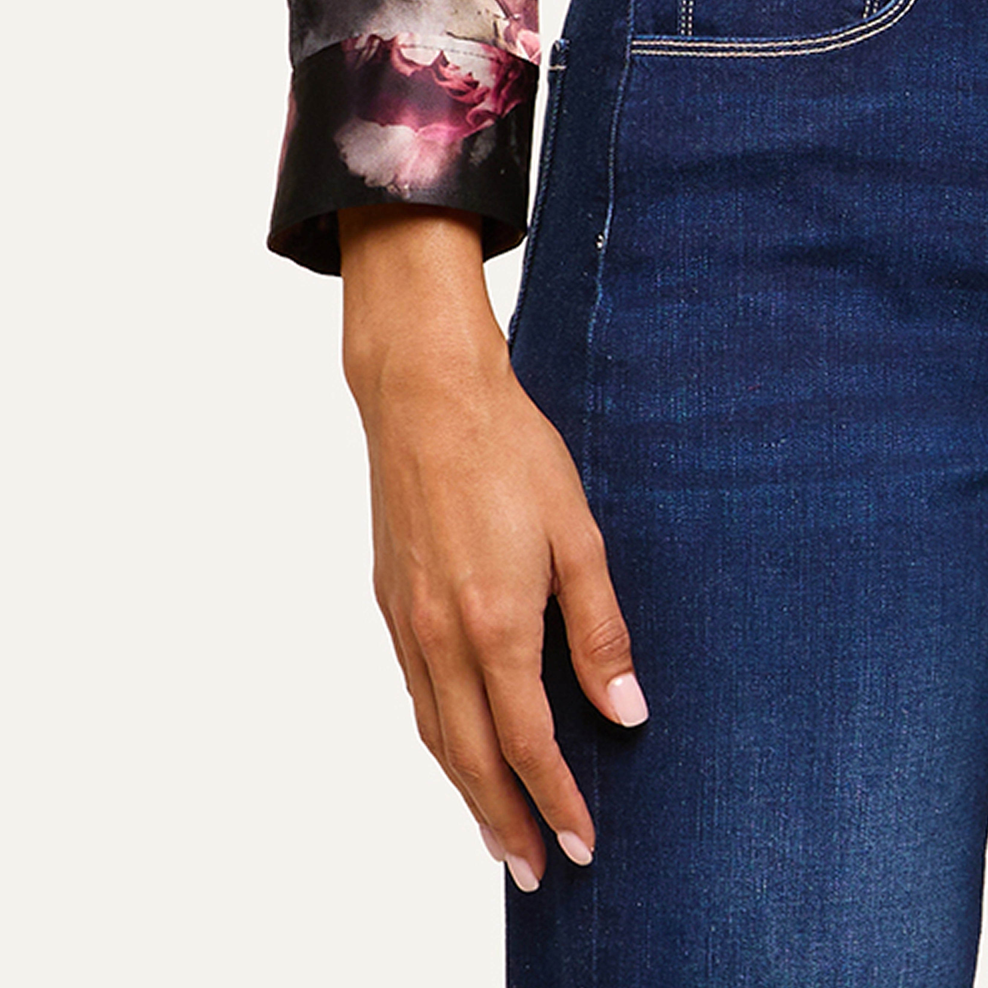 A person wearing a dark floral long-sleeve top and blue jeans, with only their left hand and part of their torso visible against a plain background.