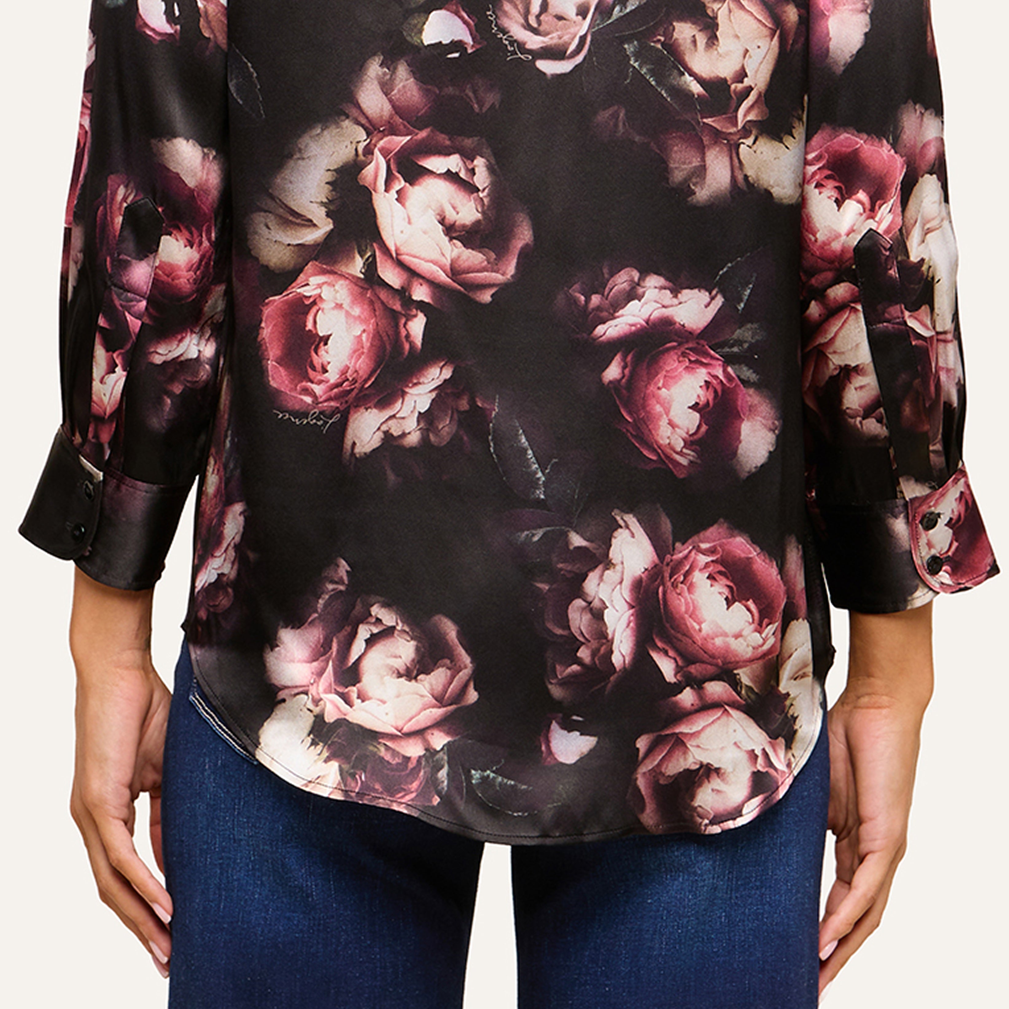A person shown from the back wears a black long-sleeve shirt with pink floral prints and blue jeans.
