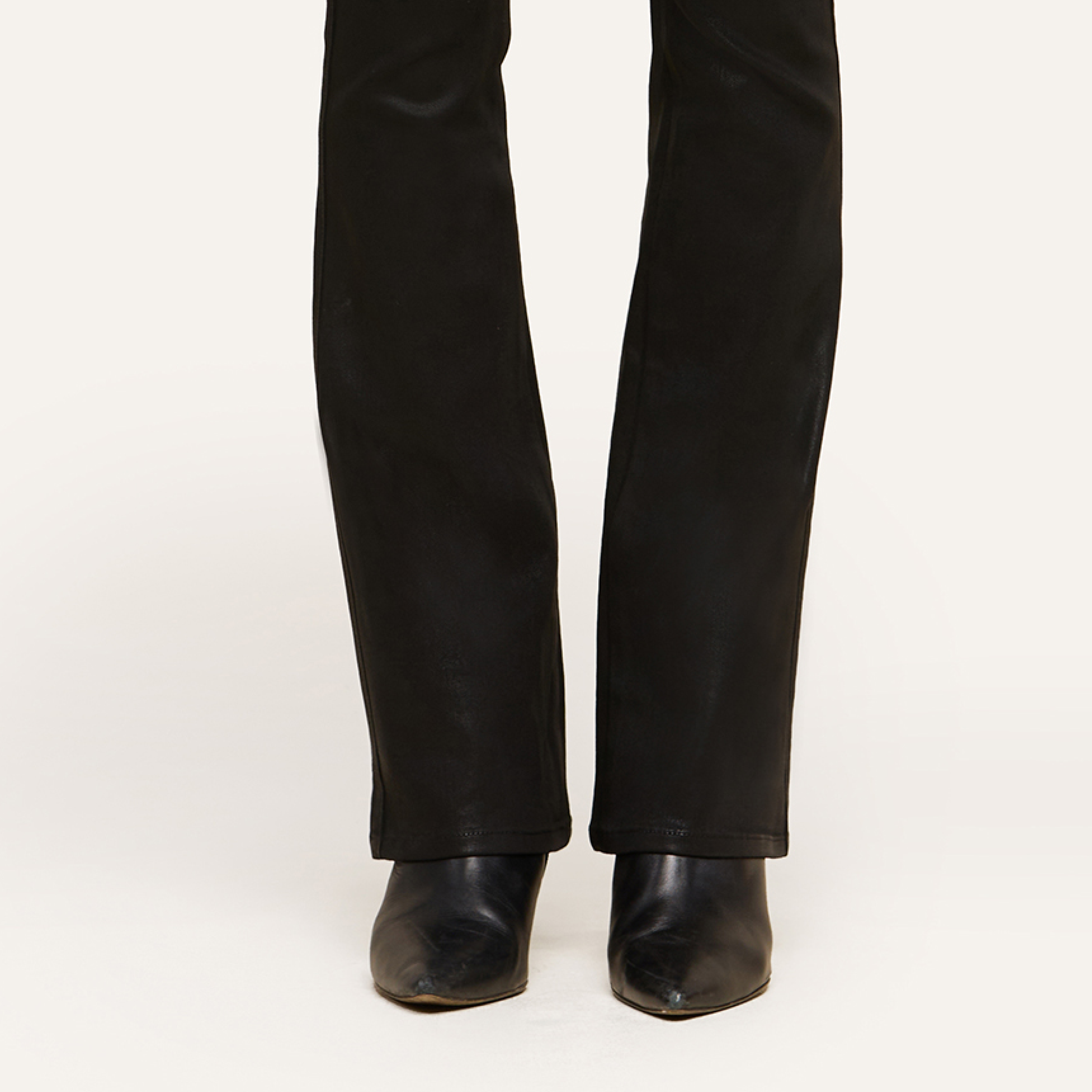 A person wearing black leather boots and black pants, shown from the knees down, stands confidently on a light-colored surface.
