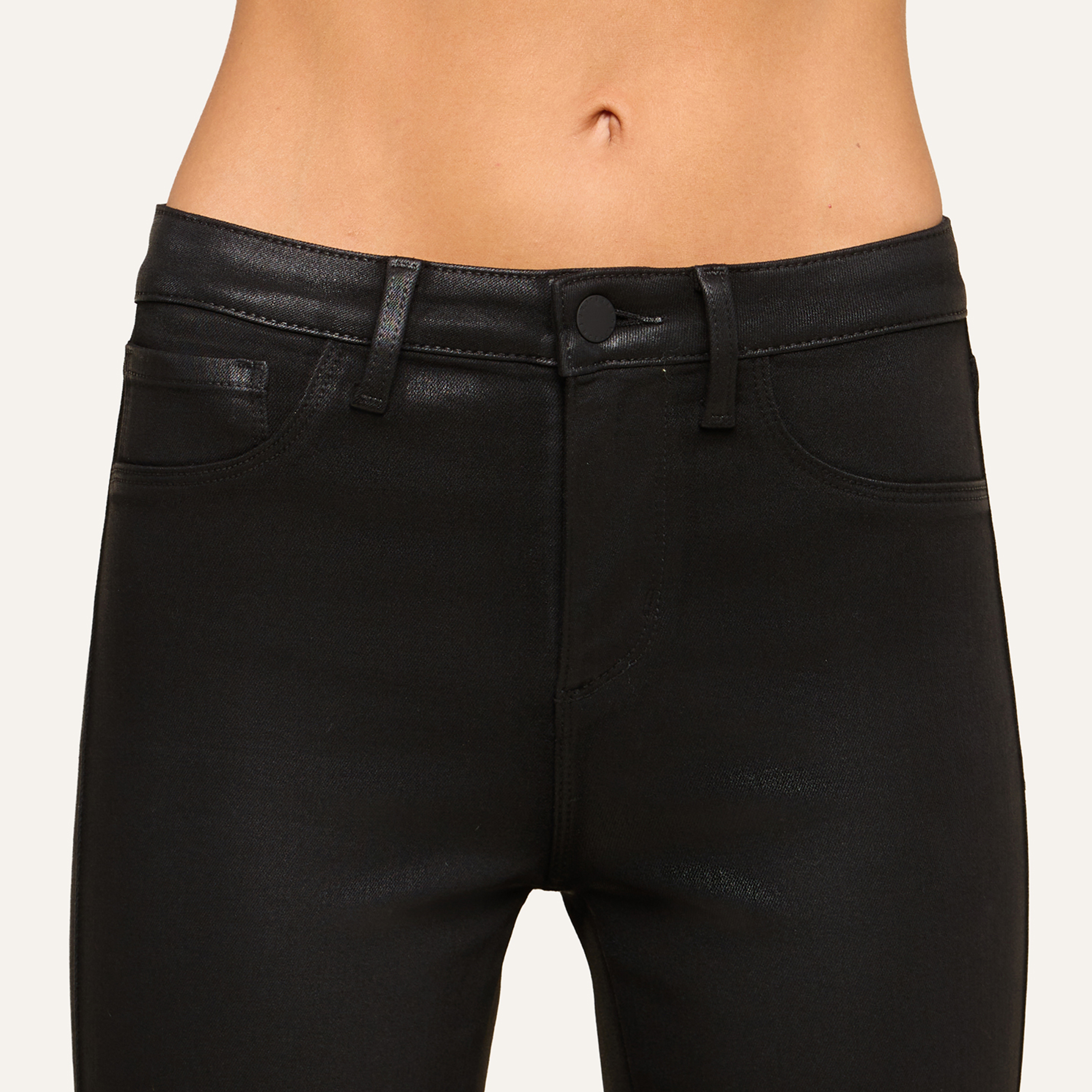 A close-up of a person’s lower torso showcases fitted, glossy black jeans with belt loops and pockets, shown from waist to mid-thigh.