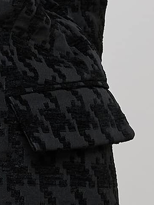 Close-up of a black fabric with a textured houndstooth pattern, featuring a flap that appears to be part of a pocket, against a plain light background.