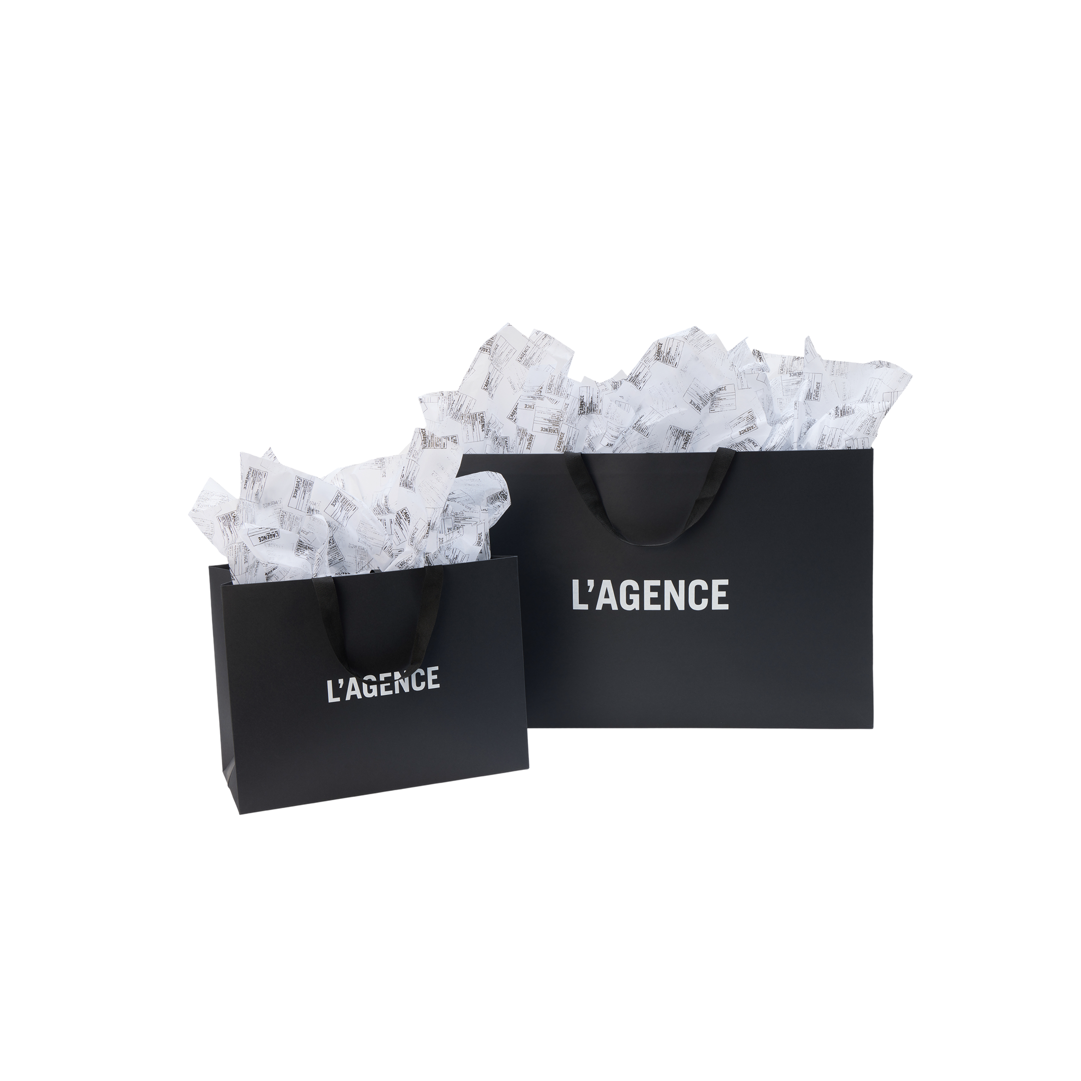 A large and a medium Gift Bag by L’AGENCE in black with white logo text and black ribbon handles, filled with white tissue paper.