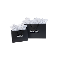 A large and a medium Gift Bag by L’AGENCE in black with white logo text and black ribbon handles, filled with white tissue paper.