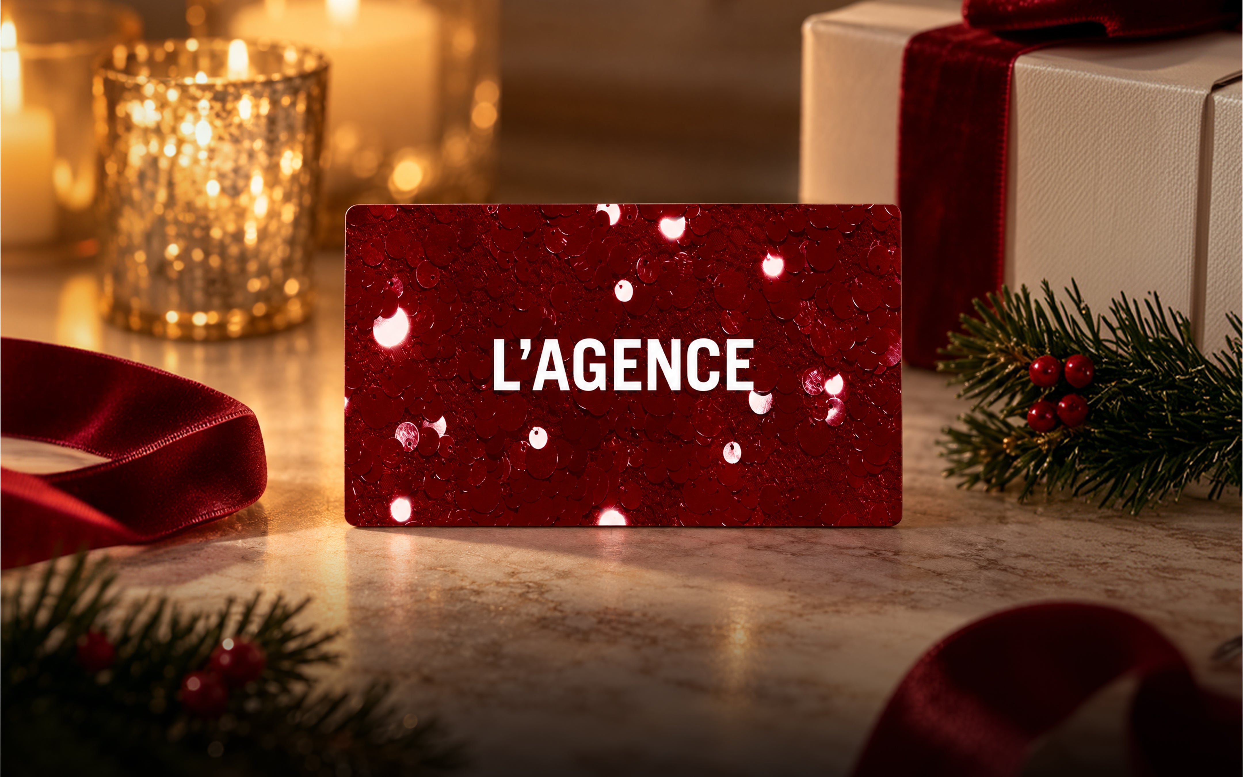 A rectangular red LAGENCE gift card surrounded by a festive gift box, candles, and evergreen sprigs.