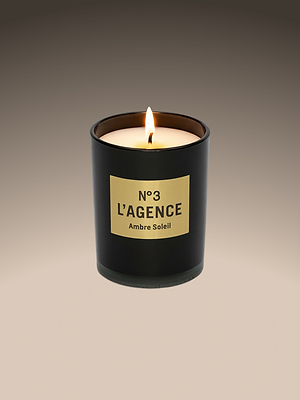 A lit Ambre Soleil soy-blend candle in a matte black jar sits against a beige-brown gradient backdrop, capturing the hand-poured, Southern California-inspired essence.
