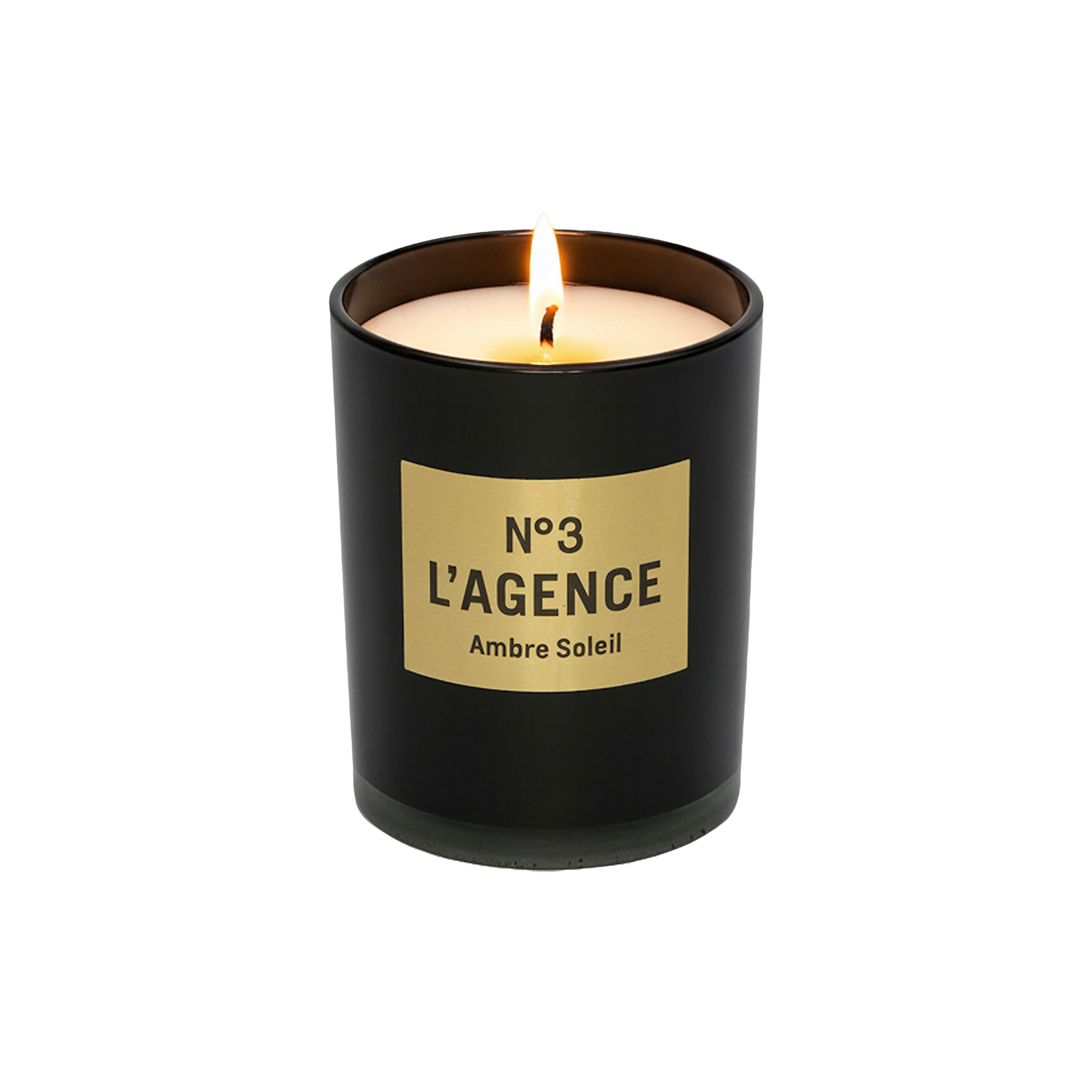 A lit, hand-poured Ambre Soleil candle in a black glass holder with a gold label sits elegantly on a plain white background. Crafted from carbon neutral soy-blend wax, this candle promises a long burn time while adding warmth and sophistication to any space.