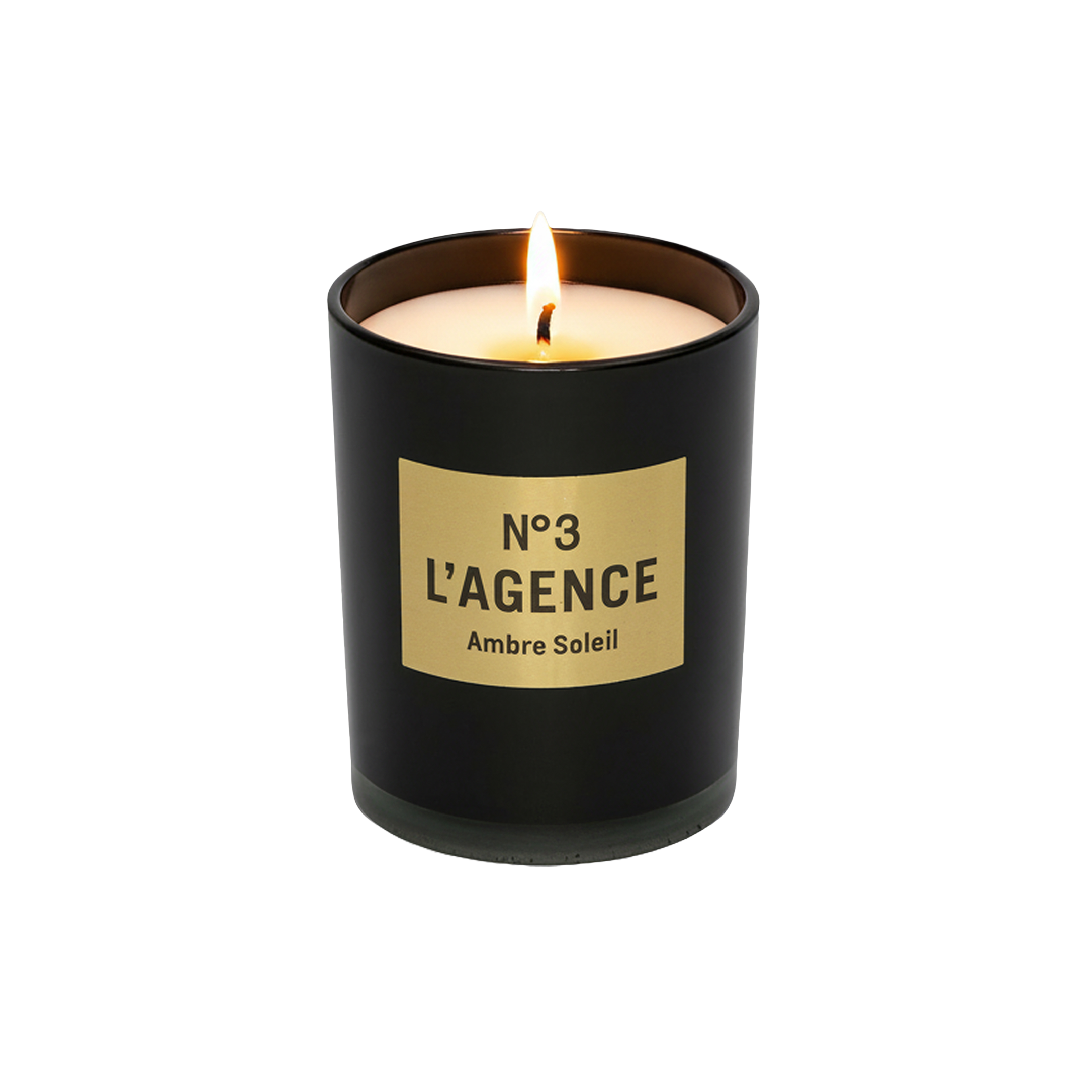 A lit, hand-poured Ambre Soleil candle in a black glass holder with a gold label sits elegantly on a plain white background. Crafted from carbon neutral soy-blend wax, this candle promises a long burn time while adding warmth and sophistication to any space.