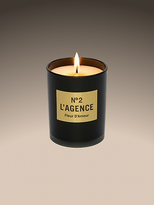 A lit Fleur DAmour candle in a matte black glass holder with a beige N°2 LAGENCE label, made from soy-blend wax, is displayed against a gradient brown background.