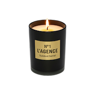 A lit Suède et Santal black sandalwood candle, crafted from soy-blend wax and housed in a glass jar with a beige label reading “No 1 LAGENCE Suède et Santal,” sits on a white background.