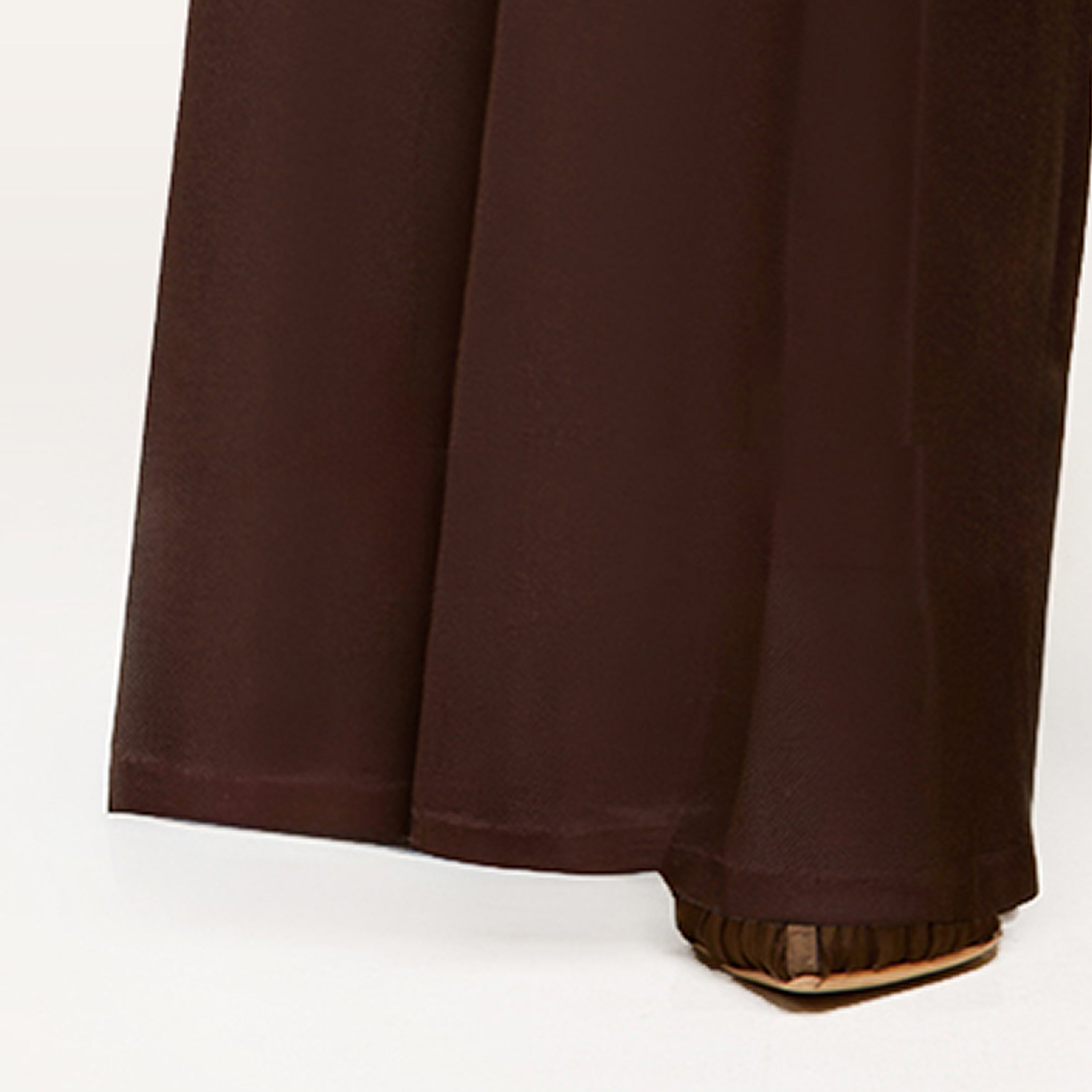 A close-up of a person wearing loose, brown linen pants that reach the ground, partially covering brown pointed-toe shoes.