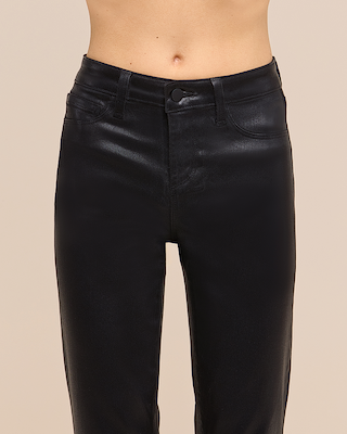 A person wearing high-waisted, shiny black pants is shown from the waist to the mid-thigh against a plain beige background.