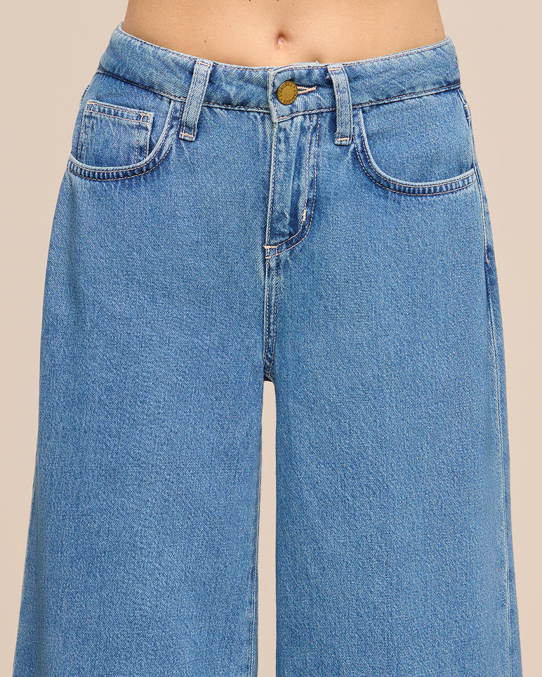A person wearing high-waisted, light blue denim jeans with wide legs. The jeans have front pockets and a button closure. Only the lower torso is visible against a plain background.