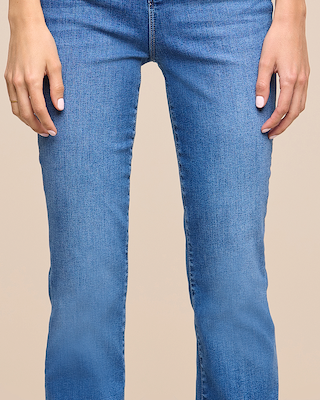 A person wearing light blue denim jeans, shown from the waist to the mid-calf, with hands resting by their sides against a plain beige background.