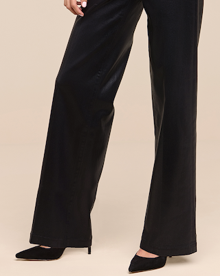 A person wearing black wide-leg pants and black pointed-toe heels stands on a beige background. Only the lower half of the body is visible.