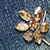 A floral gold-toned gemstone brooch rests against a textured denim fabric.