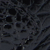 Close-up of a dark, textured surface with an irregular, honeycomb-like pattern and overlapping, webbed or netted elements. The image features shades of black and gray.