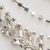 A close-up of a delicate necklace with silver and gold metallic charms and beads arranged on a light background.