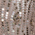 Close-up of a fabric covered with shiny, round sequins in shades of silver and gold, creating a sparkling and textured appearance.