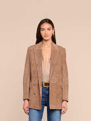 A woman stands facing forward, wearing the Arabell Romper. She has long brown hair, gold hoop earrings, and a neutral expression against a plain beige background.