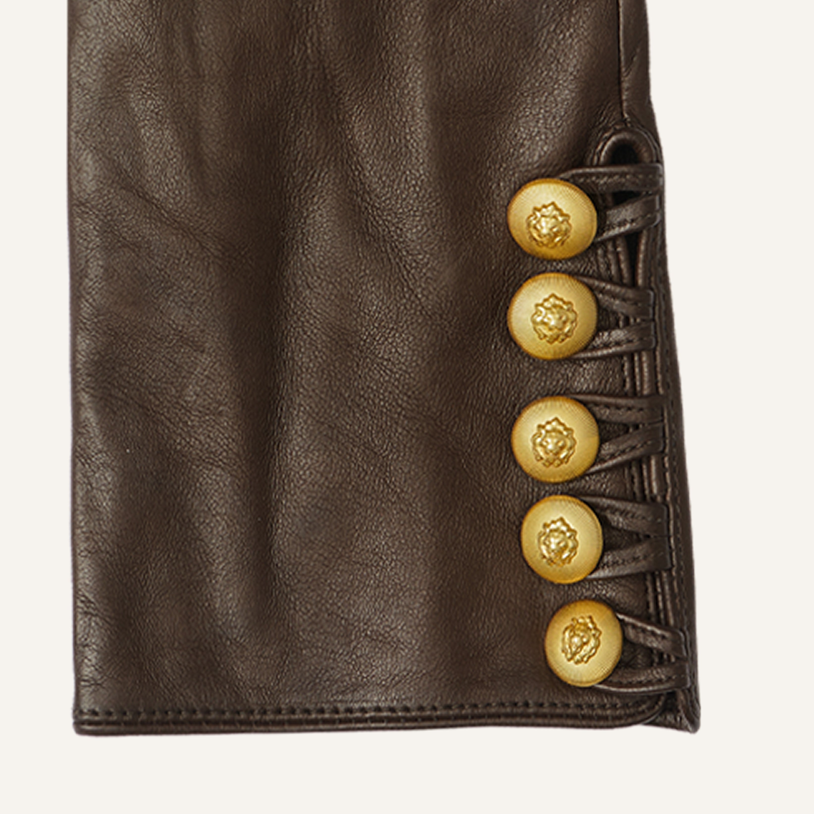 Close-up of a brown leather sleeve featuring five ornate gold buttons arranged in a vertical line along the edge, each button decorated with an embossed lion’s head motif.