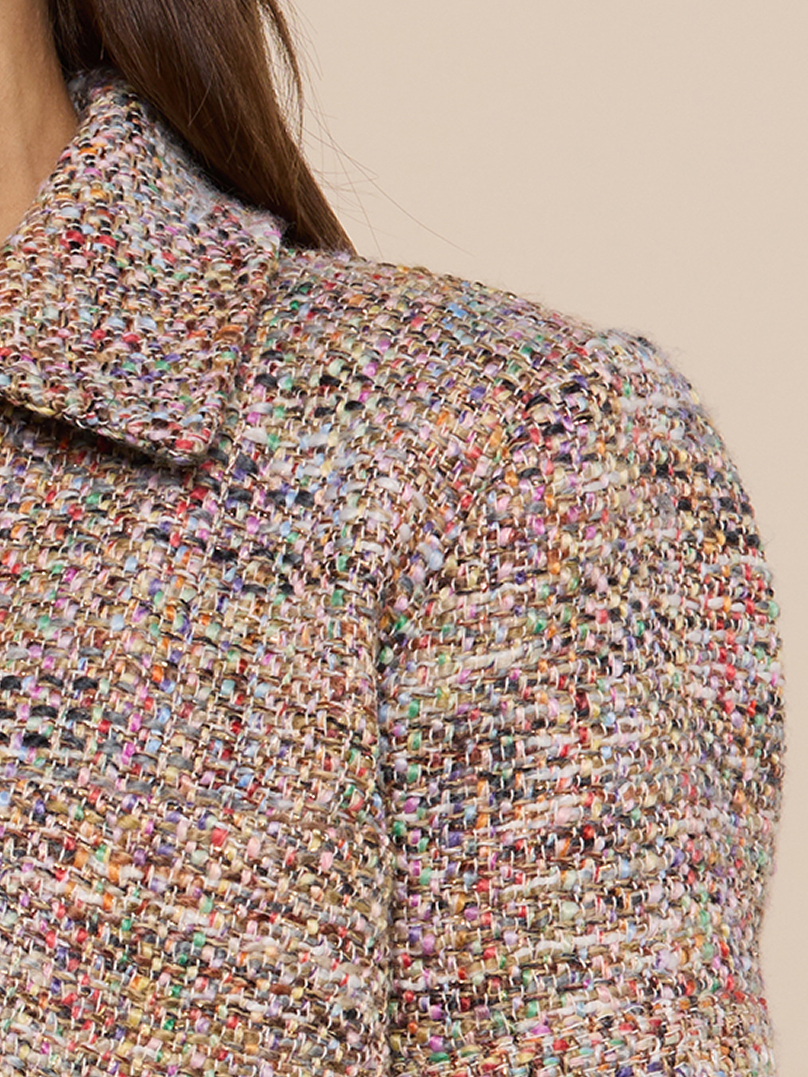 Close-up of a womans shoulder and upper arm wearing a multicolored tweed jacket with a collar, showing the textured fabric in shades of beige, pink, blue, and green.