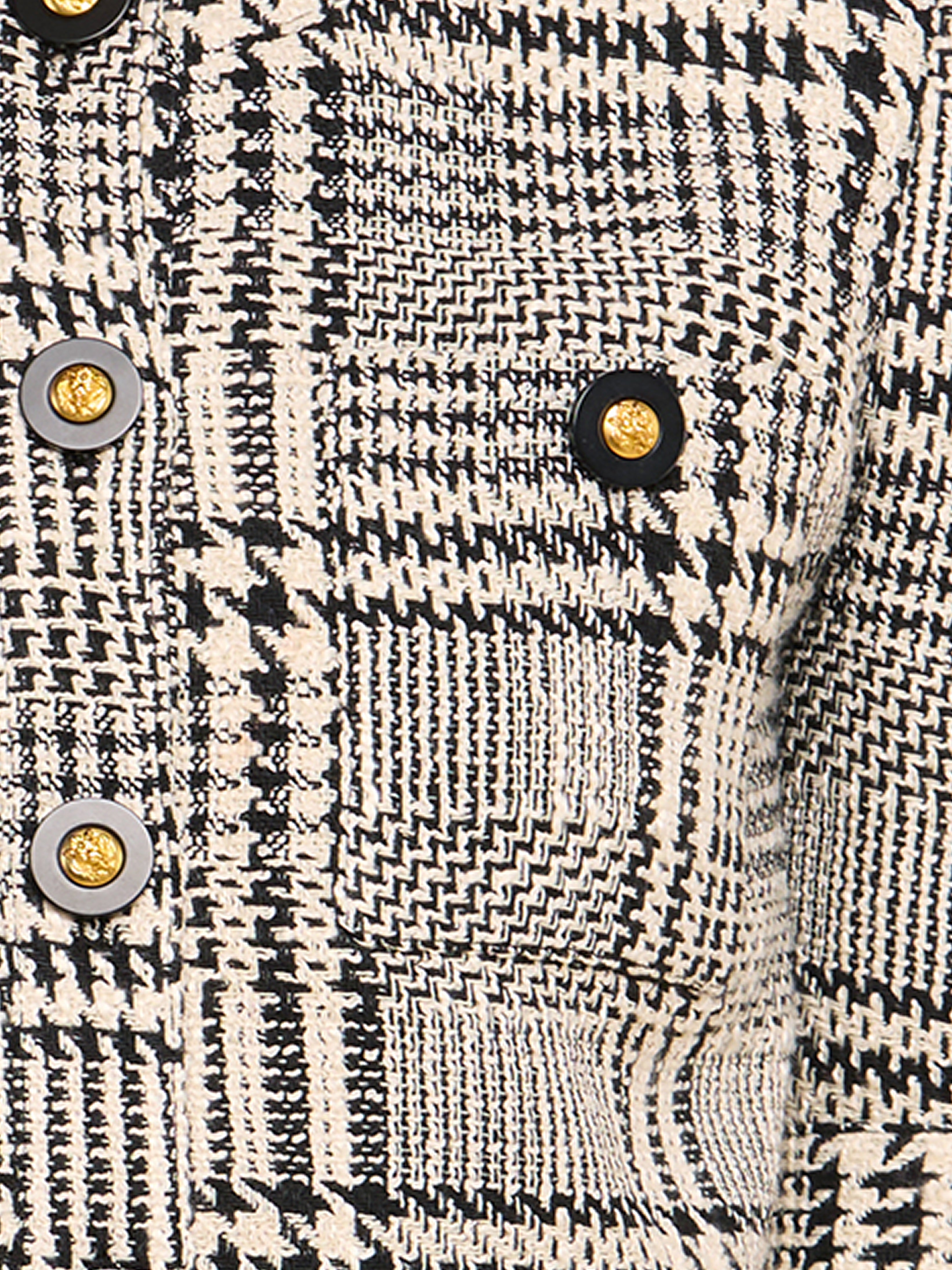 Close-up of a black and white plaid-textured fabric with gold and black decorative buttons, showing a detailed woven pattern and part of a pocket.