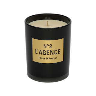 A black candle jar labeled N°2 LAGENCE Fleur D’Amour with a gold label is shown from the front against a plain white background. This elegant piece features hand-poured candles crafted from soy-blend wax and infused with the enticing scent of baccara rose.