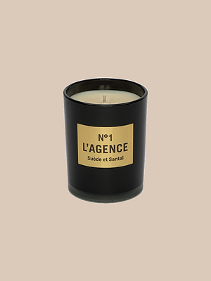 A black glass candle holder with a beige “Suède et Santal” label holds light soy-blend wax scented with sandalwood, all set against a plain beige background.