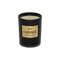 A black candle jar labeled Suède et Santal, adorned with a tan rectangular label and an unlit wick, is displayed against a plain white background. This elegant candle is crafted from a soy-blend wax and features the sophisticated scent of sandalwood.