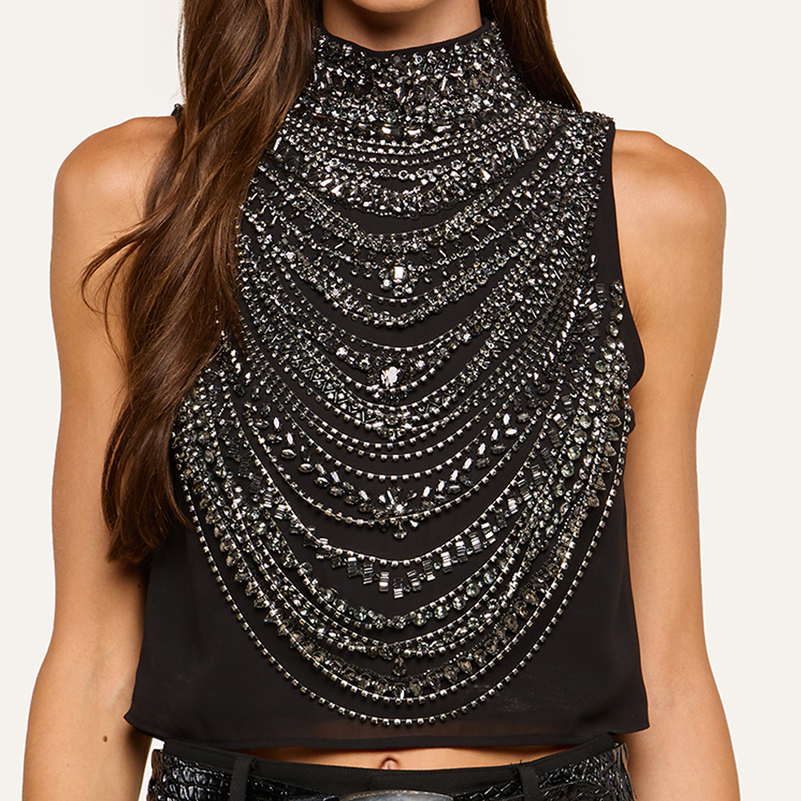 A woman wears a sleeveless black top adorned with intricate, layered silver beading and rhinestones, creating a statement, glamorous look with dazzling embellishments.