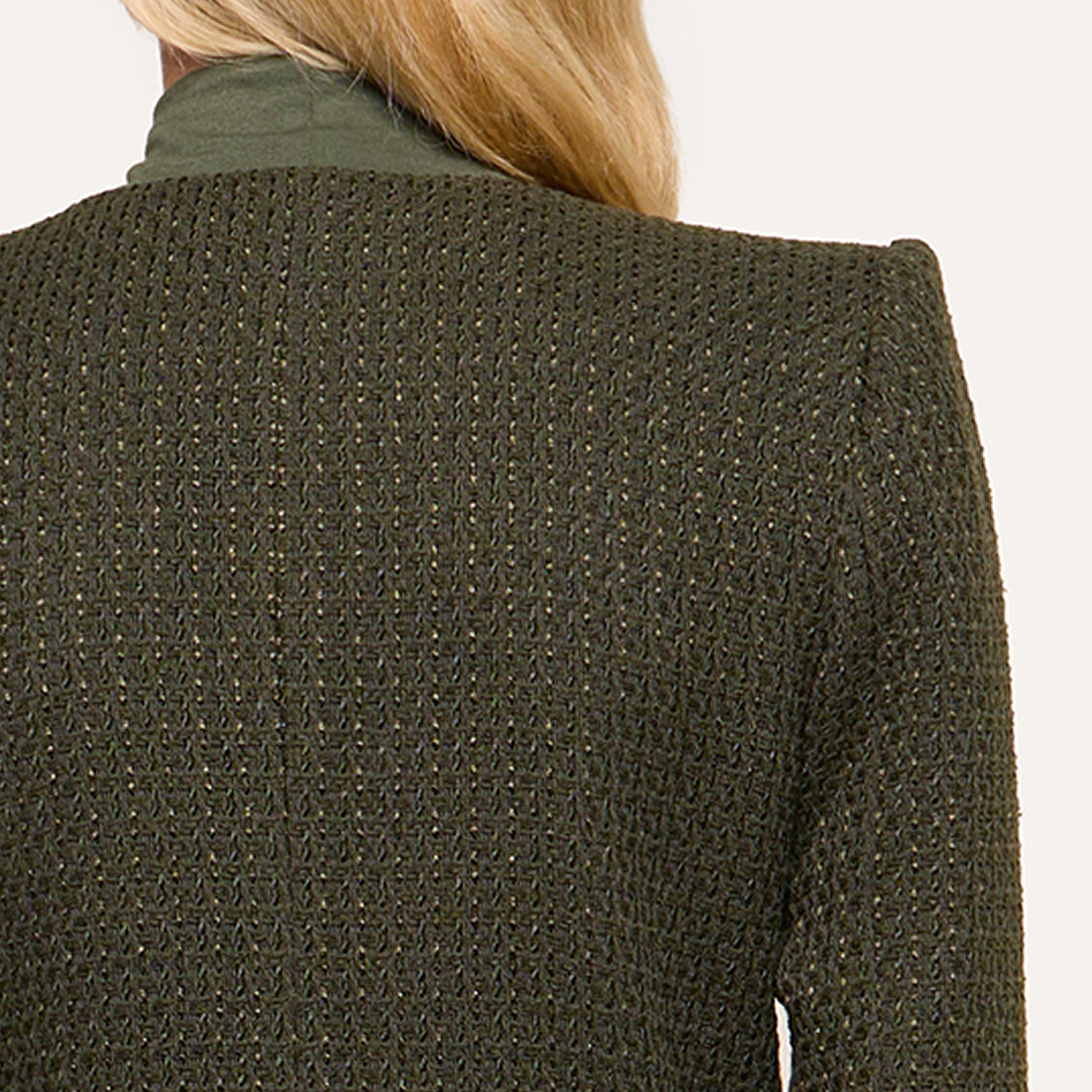 The image shows the back view of a person wearing a textured dark green jacket over a green turtleneck top. Only the upper body and part of their blond hair are visible against a plain background.